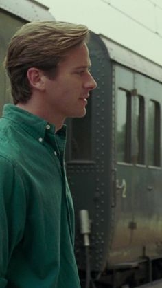 a young man standing in front of a train on the tracks, looking off into the distance