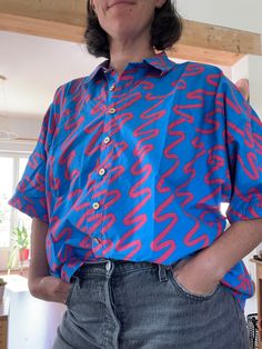 This short-sleeved cotton poplin shirt with its oversized cut flatters all figures, while its soft and breathable fabric offers incomparable comfort. The vibrant electric blue, enhanced by fuchsia geometric patterns, makes it a unique piece that attracts all eyes. The gold buttons provide a chic and elegant finish, perfect for a casual yet sophisticated look. This one-size-fits-all shirt is suitable for a wide variety of body types, creating a relaxed yet stylish effect. Ideal to wear with jeans or a skirt for a modern and original look! Short-sleeve Tops With Geometric Pattern, Cotton Poplin Shirt, Poplin Shirt, Gold Buttons, Geometric Patterns, Cotton Poplin, Body Types, Womens Clothing Tops, Electric Blue