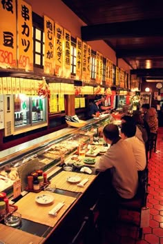 people sitting at tables in a restaurant with food on the counter and signs above them