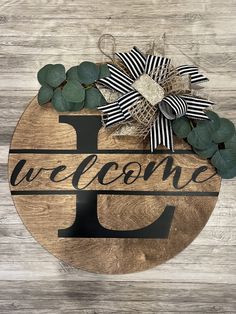 a wooden sign with the word welcome hanging on it's side, decorated with greenery