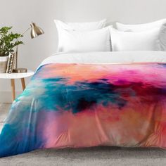 a bed covered in a colorful comforter next to a night stand with a plant