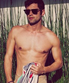 a shirtless man is holding several towels and looking off to the side while standing in front of tall grass