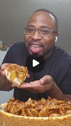 a man holding a piece of food in front of a cake with nuts on it