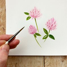 a person holding a paintbrush and drawing pink flowers on paper with watercolor pencils