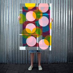 a person holding up a large piece of art with circles painted on the side of it