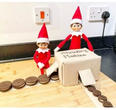 two elfs are standing next to a box with cookies on it