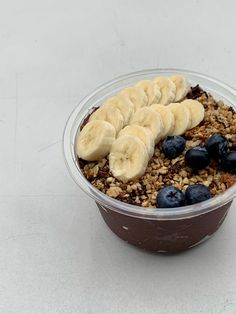 a bowl of granola with bananas and blueberries in it on a white surface