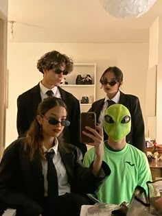 three people in business attire are taking a selfie with an alien mask