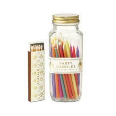 a jar filled with lots of colorful candles next to a box of matchesticks