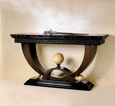 a wooden table with a marble top and two balls on the base, against a beige wall