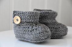 a pair of gray crocheted baby boots with a wooden button on the side