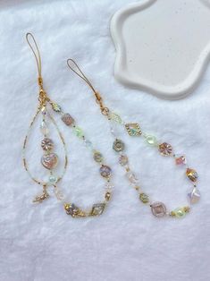 two pairs of earrings sitting on top of a white blanket next to a bowl and spoon