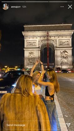 two girls standing in front of the arc de trioe at night with their hands up