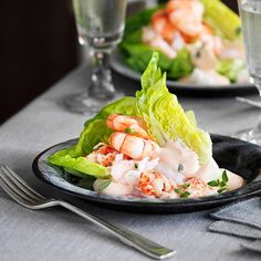 a black plate topped with lettuce and shrimp on top of a white table cloth