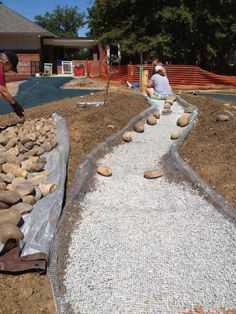 two men are working on landscaping in the yard with rocks and gravel laid around them