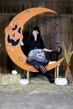 a woman sitting on a bench in front of a fake moon with bats and pumpkins