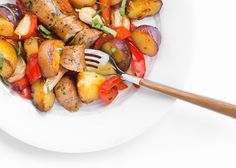 a white plate topped with meat and veggies next to a wooden utensil