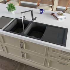 two black sinks sitting on top of a white counter next to chairs and a potted plant