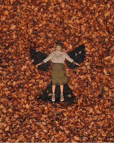 a woman laying on top of leaves in the middle of a field with her arms spread out