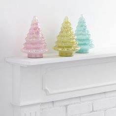 three glass christmas trees sitting on top of a mantle