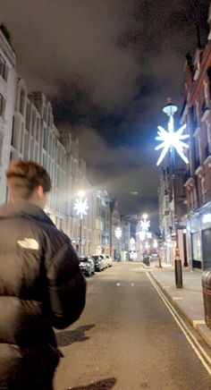 a man is walking down the street at night with his back turned to the camera