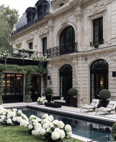 a large house with a pool in front of it and lots of white flowers on the lawn