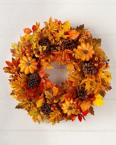 a wreath with autumn leaves and pine cones hanging on a white brick wall in front of a door