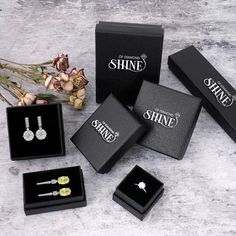 four different types of earrings in black boxes on a white table next to flowers and a bouquet