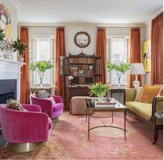 a living room filled with furniture and a fire place in front of two windows covered in orange drapes