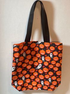 an orange and black tote bag with halloween pumpkins printed on the side, hanging from a hook