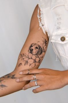 a woman's arm with a dog and flowers tattoo on the left side of her arm