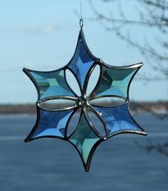 a stained glass star ornament hanging from a tree in front of the water