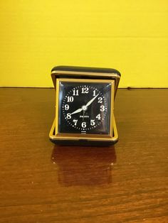 a small clock sitting on top of a wooden table next to a yellow wall and floor