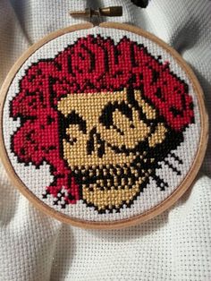 a cross stitch skull with red hair on it's head