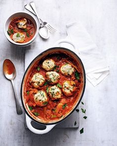 a pot filled with meatballs and sauce on top of a white table next to two spoons