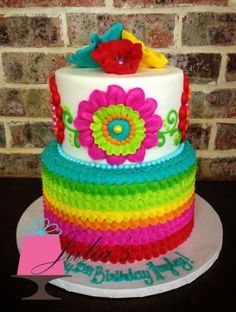 a multi - layer cake decorated with flowers and ribbons on a plate in front of a brick wall