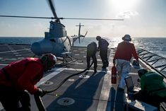 several people are on the deck of an aircraft carrier with a helicopter in the background