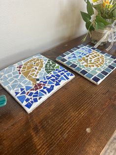 two pieces of colorful tile sitting on top of a wooden table next to a vase with flowers