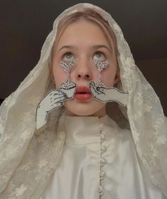 a woman with painted hands on her face is wearing a white dress and veil over her head