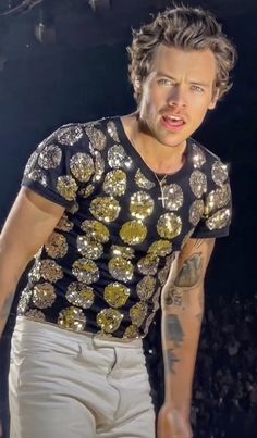 a man with tattoos on his arm and wearing a black t - shirt that has gold sequins on it