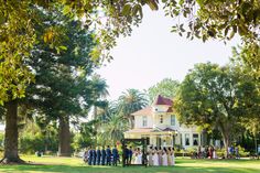 a group of people standing in front of a white house on a lush green field