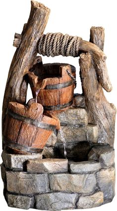 a water fountain made out of wood and rope with buckets on the side, sitting next to rocks