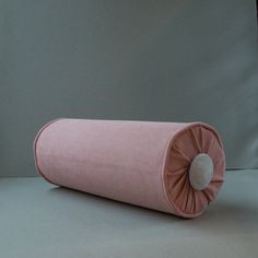 a pink pillow sitting on top of a white floor next to a wall with a clock in the background