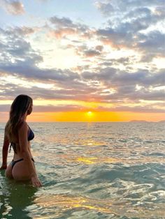 a woman is sitting in the water at sunset with her back turned to the camera