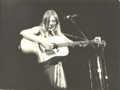 a woman holding a guitar while standing in front of a microphone