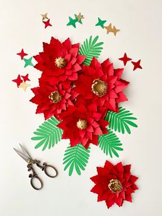 paper poinsettis and scissors on a white surface with stars in the background