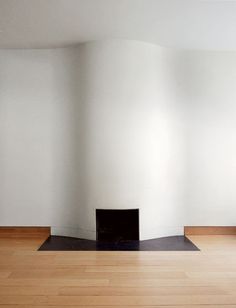 an empty room with wood floors and white walls, including a fireplace in the corner