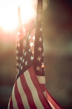 an american flag hanging from a pole with the sun in the back ground behind it