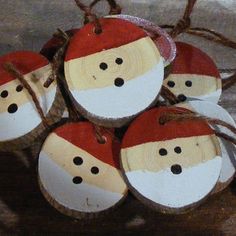 four wooden ornaments with faces on them are sitting on a piece of wood, hanging from a string