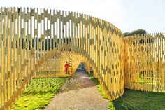 a wooden structure in the middle of a grassy area with people walking on it and one person standing at the end